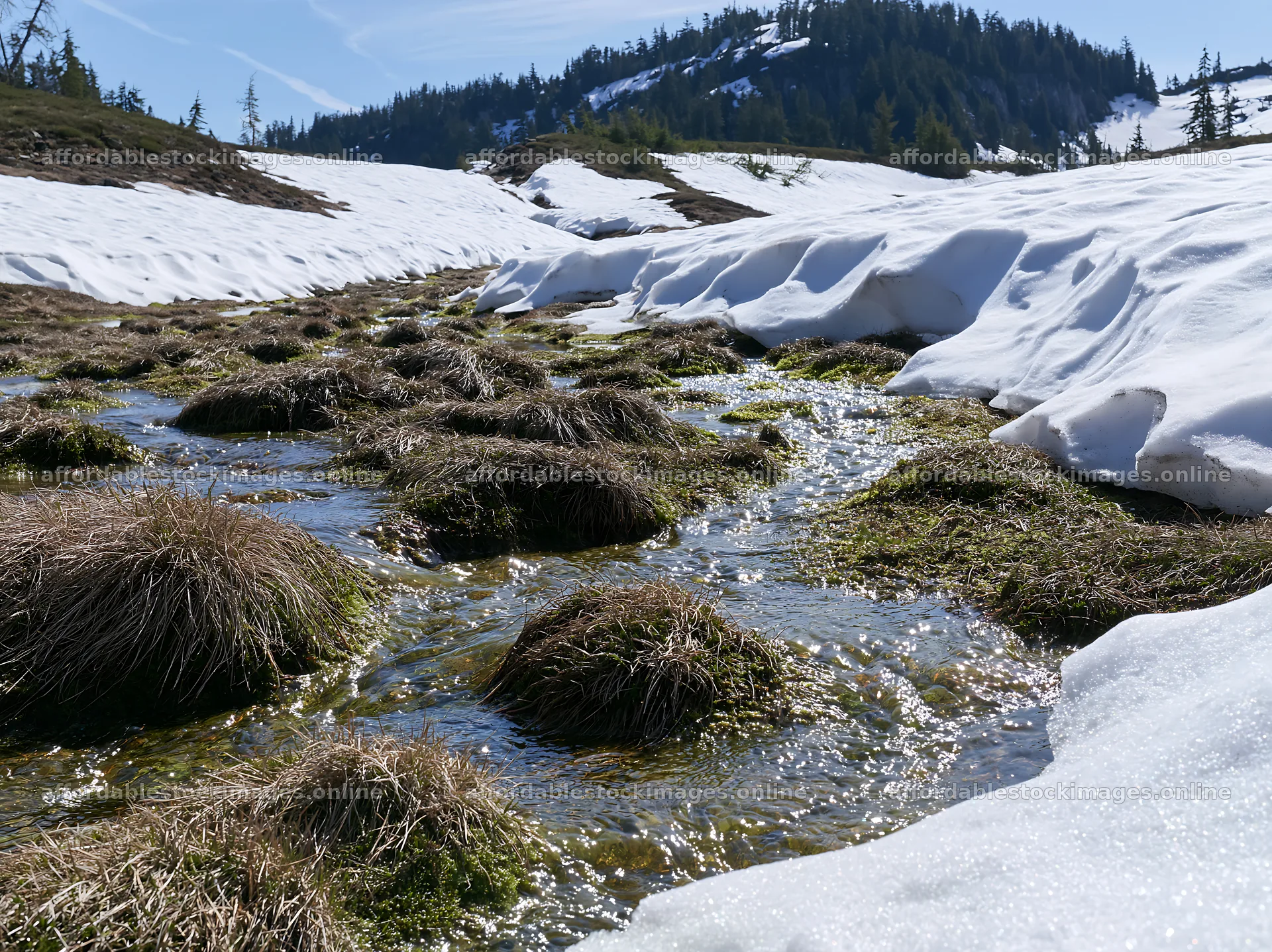Snowmelt flowing through a meadow with patches of grass – stock images 9174x6866
