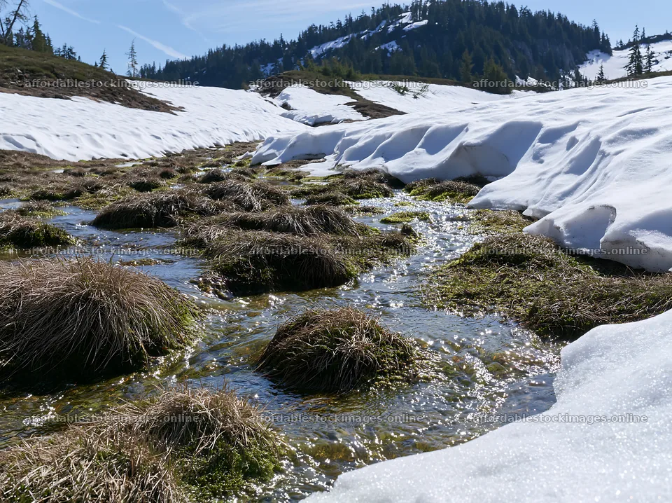 Snowmelt flowing through a meadow with patches of grass – stock images 9174x6866