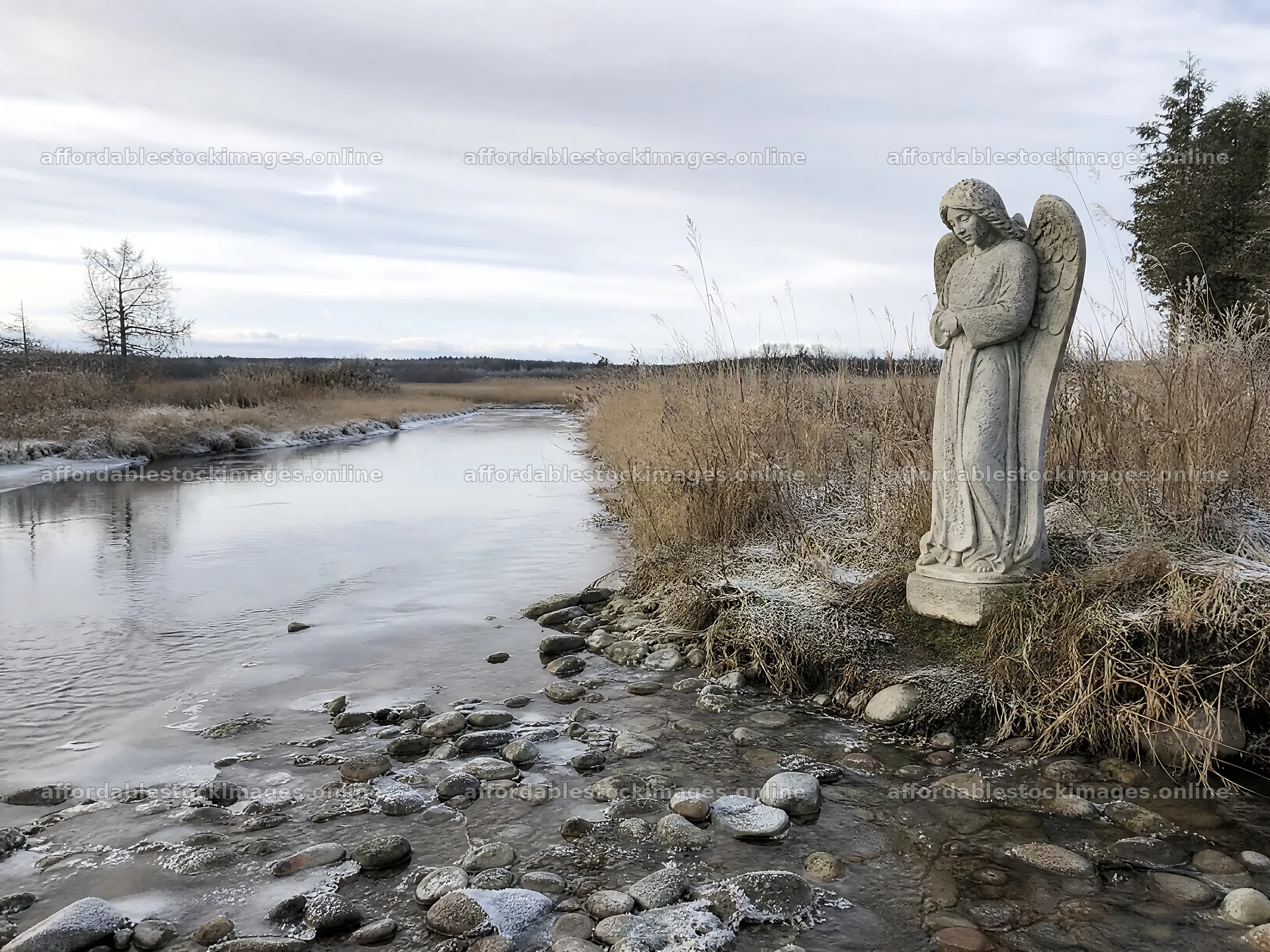 Winter angel statue in a meadow by a stream – stock images 9166x6874