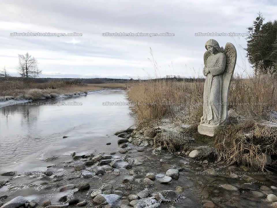 Winter angel statue in a meadow by a stream – stock images 9166x6874