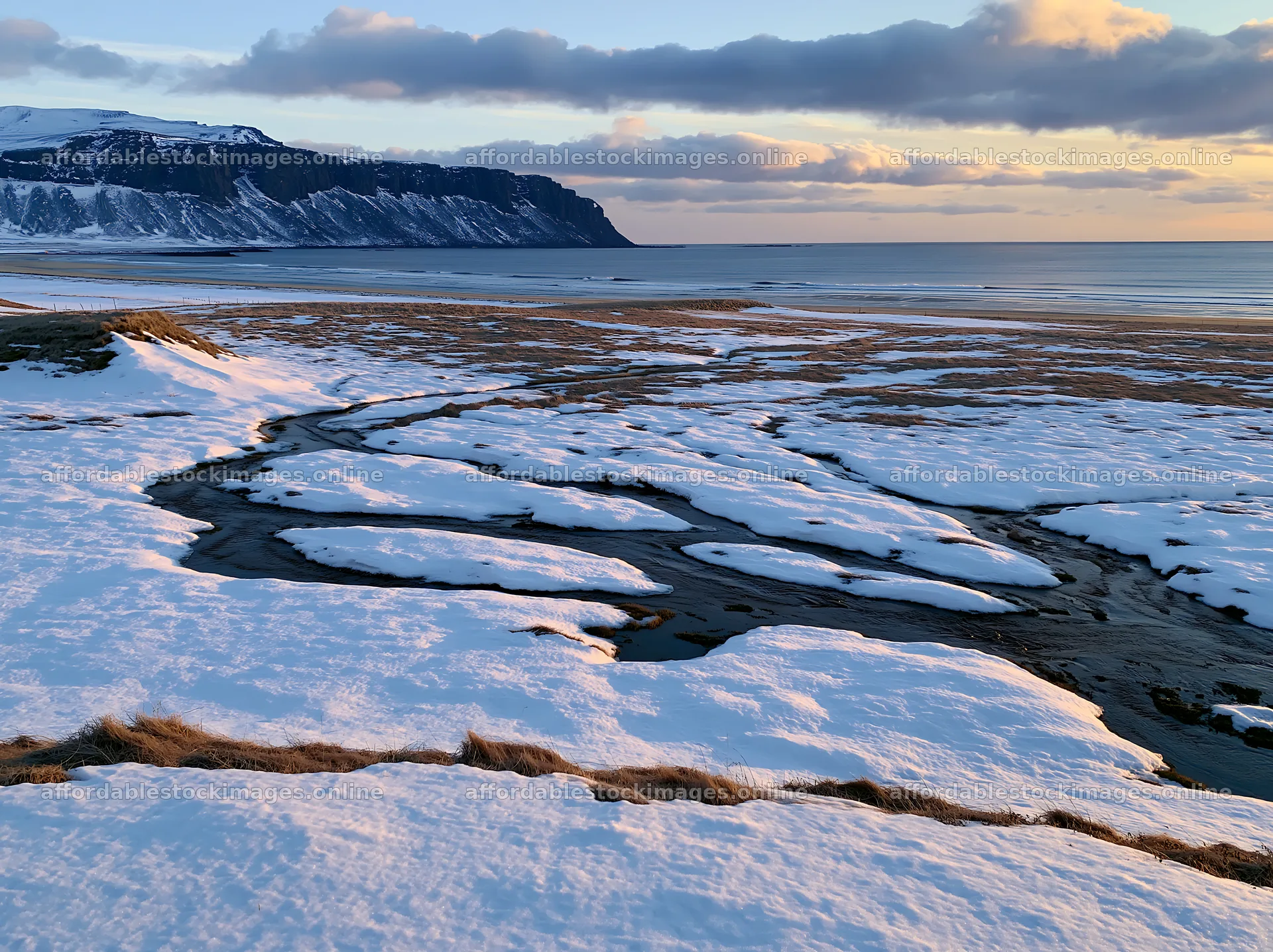 Snowbound meadow with flowing stream and cliffs in background – stock images 9174x6866
